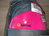 Close-up of the Gemys embroidered logo on the pink fabric of the jacket.