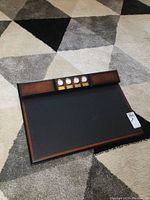 Top-down view of Bombay desk writing pad showing black writing surface, wood frame with burl finish, and row of four clocks with brass labels along rear edge.