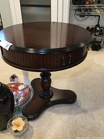 Front view of round pedestal table with fluted sides and storage compartment handles.