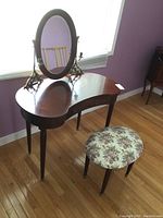 Full view of Bombay vanity with kidney-shaped top, large oval mirror, and floral upholstered stool sitting on hardwood floor.