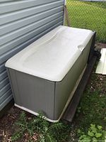 Side view of grey plastic deck box with white lid positioned against siding on wooden planks