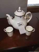 Front view of teapot with four demitasse cups set around it on wood surface, showing size and design details