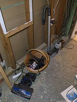 Dyson vacuum accessories including motorized brush head, extension tubes, and basket of smaller items, on basement floor.