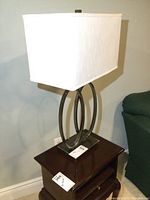 Full view of one metal table lamp with rectangular shade on dark wood side table near green couch.