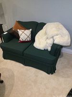 Front view of the dark green upholstered loveseat with cushions and white throw.