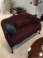 Front view of burgundy upholstered vintage loveseat with wooden legs and matching cushions, showing fabric texture and design.