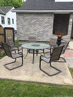 Full view of round glass top table and six sling chairs on patio