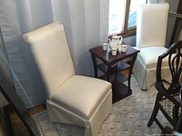 Pair of cream striped upholstered slipper chairs shown beside each other near small side table, showing upholstery and size.