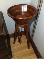 Full view of the wooden salad bowl sitting on its three-legged wooden stand, showing its overall shape and finish.
