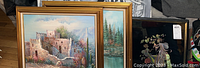 Three framed artworks stacked, including two landscape canvas reproductions and one fairy-themed framed art