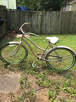 Full side view of cruiser bicycle on grass, showing curved frame, saddle, wheels with green rims and white fenders, and handlebar with green accents