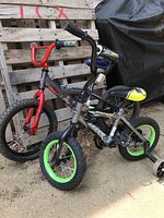 Two children's bicycles together, one smaller with training wheels, the other larger with red front forks.