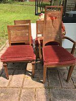 Photo of four dining chairs outdoors; chairs have wooden frames, red padded seats, and cane backs; one chair has a torn cane panel.