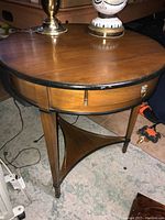 Full round wooden entry table with brass pull drawer, visible nicks, scratches and base damage.