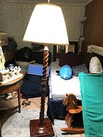 Wooden floor lamp with twisted column design and white lampshade in a room with various furniture.