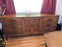 Full front view of mid-century modern buffet with six drawers and double cabinet doors, wood stained and visible wood grain under natural light, positioned with curtain background.