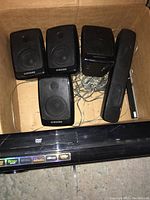 Samsung surround sound system components in a cardboard box including four small speakers, one center channel speaker, and main control unit.