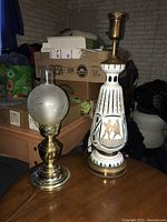 Two table lamps pictured together, one oil lamp with frosted glass globe and brass base, another taller decorative ceramic lamp with brass fittings.