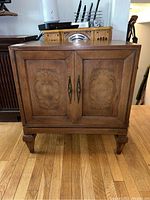 Front view of the wooden server cabinet showing two paneled doors with metal handles and tapered legs.