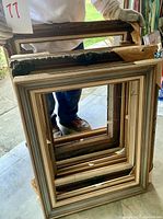 Photo showing multiple stacked wood picture frames in various sizes and finishes, held upright by a person wearing gloves.