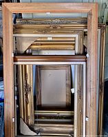 Multiple wood picture frames stacked, showcasing varied sizes and gold/brown finishes without glass.