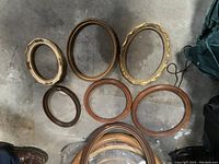 Top-down view of seven assorted oval frames, varying in size and style, laid on a concrete floor.