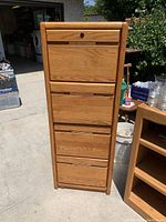 Front view of tall wood file cabinet with four drawers, lock, and natural wood finish.
