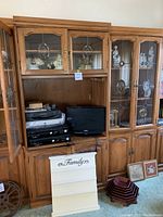 Front view of the wood display cabinets showing glass doors, brass hardware, and lighting inside. Cabinets contain figurines and electronics placed inside and nearby.
