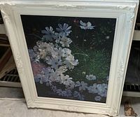 Framed acrylic painting of white flowers against a dark background in an ornate white frame