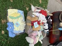Two bins filled with assorted baby clothes (onesies and crochet hats) and multiple teddy bears including a green frog plush and other stuffed animals.