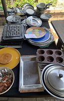 Overview of cooking and baking items, including trays, pots, pans, platters and a cupcake mold, arranged on table.