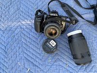 Minolta SLR film camera body with attached lens, separate telephoto zoom lens, Minolta lens cap on moving blanket