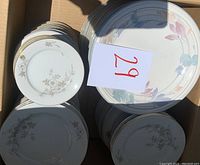 Box containing stacks of small coffee cup saucers and various plates with floral designs and gold rim edges, photo shows set from the top-down view.