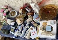 Wide shot showing the majority of items included: assorted ceramic figurines including statues of people and horses, a light house, colorful flowers, a large amber colored glass platter, various vases, coasters, and a porcelain candle holder.