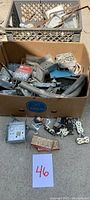 Photo showing a cardboard box filled with assorted used metal electrical boxes, outlet plugs, and some plastic face covers scattered around.