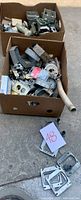 Two large cardboard boxes containing miscellaneous electrical hardware and metal pieces on a concrete floor.