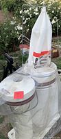 Photo of Jet DC dust collector showing dual white filter bags with red Jet branding and metal cyclone separators under protective plastic cover.