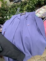 Light purple coat with buttons, laid flat on outdoor surface surrounded by other garments.