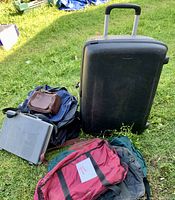 View of black Samsonite rolling suitcase, soft carrying bag, grey briefcase with brown accessory pouch, placed on grass outdoors.