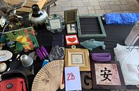 Overview photo of various items on a black tabletop including eagle statue, decorative plates, frames, fans, dolphin figure, soap dish, and other miscellaneous items.