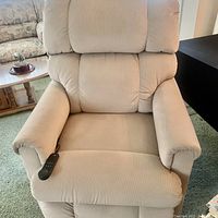 Front view of beige fabric massage recliner chair with cushioned padded design. Shows remote control laying on left armrest. Chair is in visibly good condition with minor signs of use.