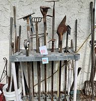 Photo of various yard tool handles inserted in a plastic rack holder against a wall.