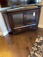 Front view of dark wood corner cabinet with two glass paneled doors, drawer at base, and a flat top with a TV stand on top (TV not included).