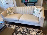 Front view of beige fabric sofa with two floral throw pillows