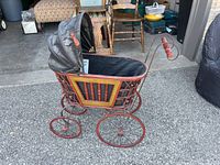 Side view of vintage doll pram showing body, wheels, and fabric canopy