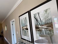 Two framed prints of water and forest scenes hung on beige wall, with reflections and soft colors.