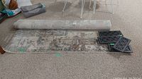 Rolled and partially unrolled area rug with four metal registers on carpeted floor.