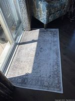 Full view of the Ruggable rug beside a chair and sliding glass door showing the faded Persian-style pattern and colors.