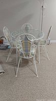 Full view of round glass top table with four metal frame chairs upholstered in blue and beige plaid fabric.