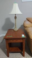 Photo showing the wood side table with single lower shelf and table lamp on top beside a couch.